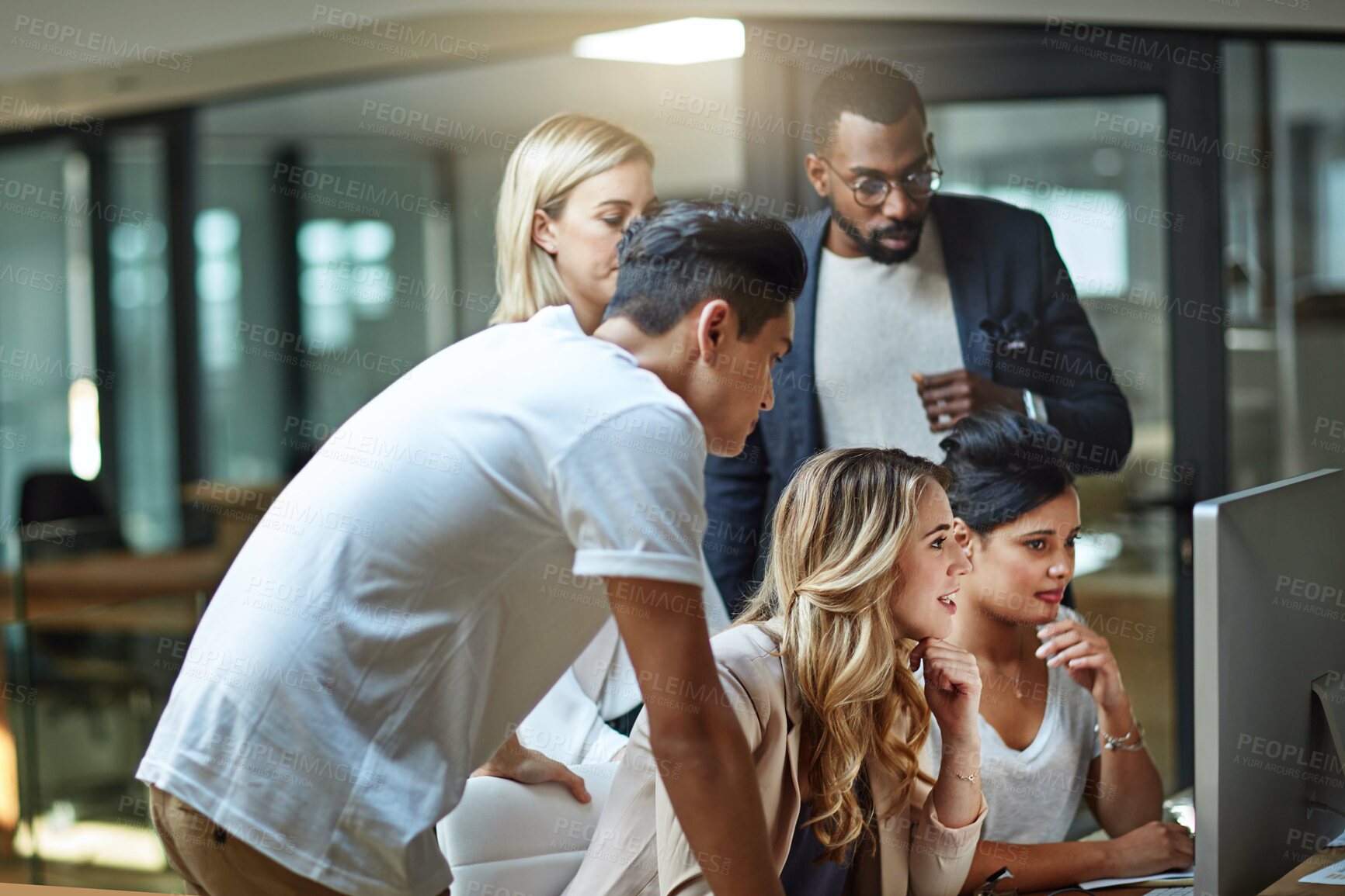 Buy stock photo Diverse team of business people looking at a computer screen together for a group project in a modern office. Young, thinking and professional men and women at a desk working on analyzing information