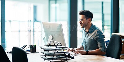 Buy stock photo Shot of a focused young businessman using a computer at his desk in a modern office