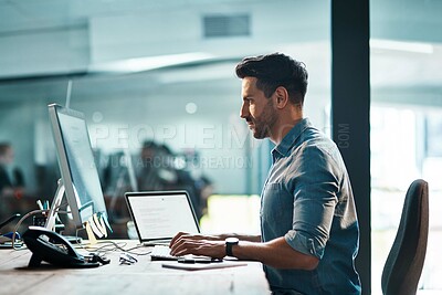 Buy stock photo Shot of a young businessman using a computer at his desk in a modern office