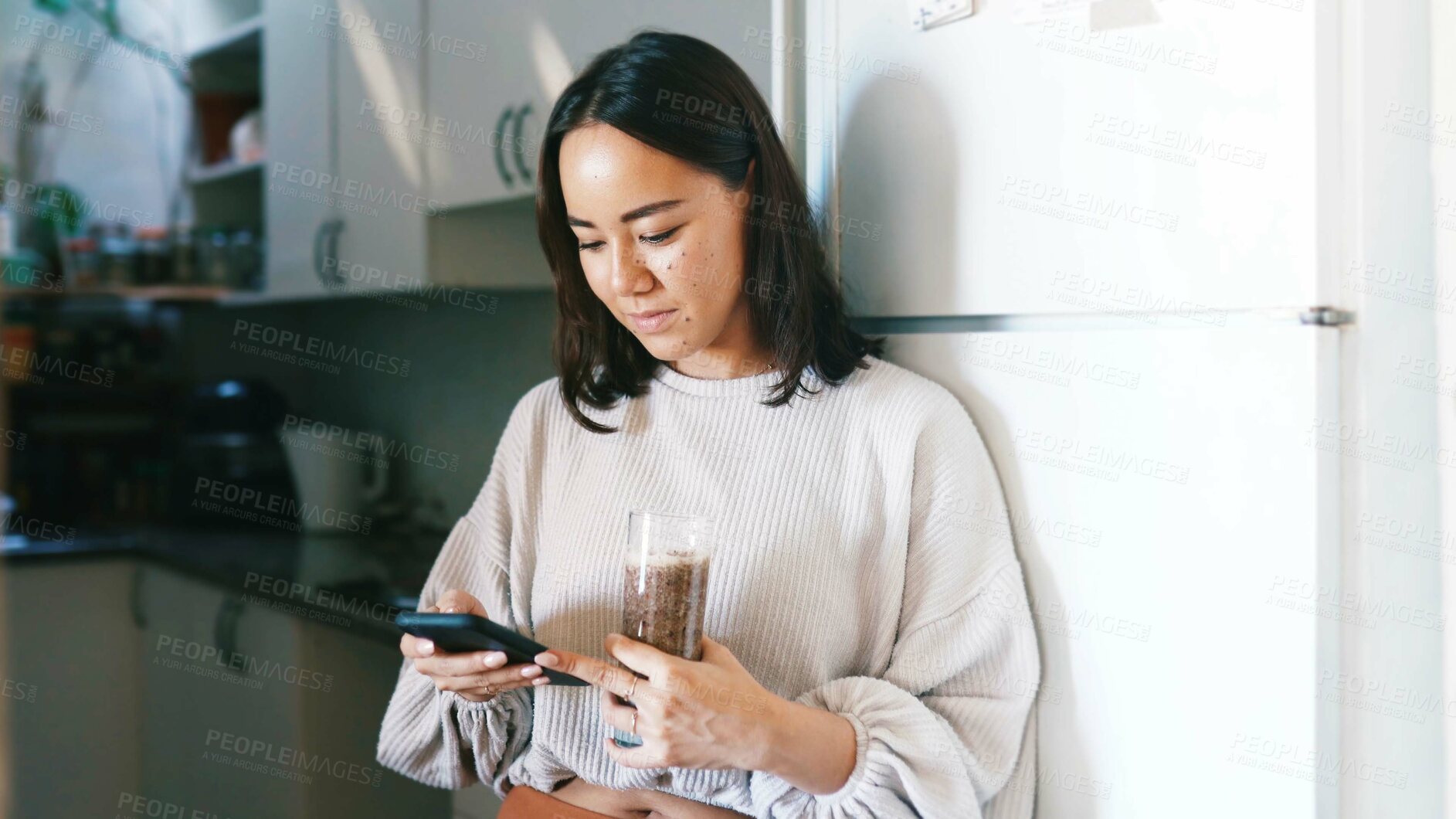 Buy stock photo Woman, phone and texting in kitchen with smoothie, drink and glass for gut health with web chat in home. Person, smartphone and scroll on mobile app, contact or social media with nutrition in house