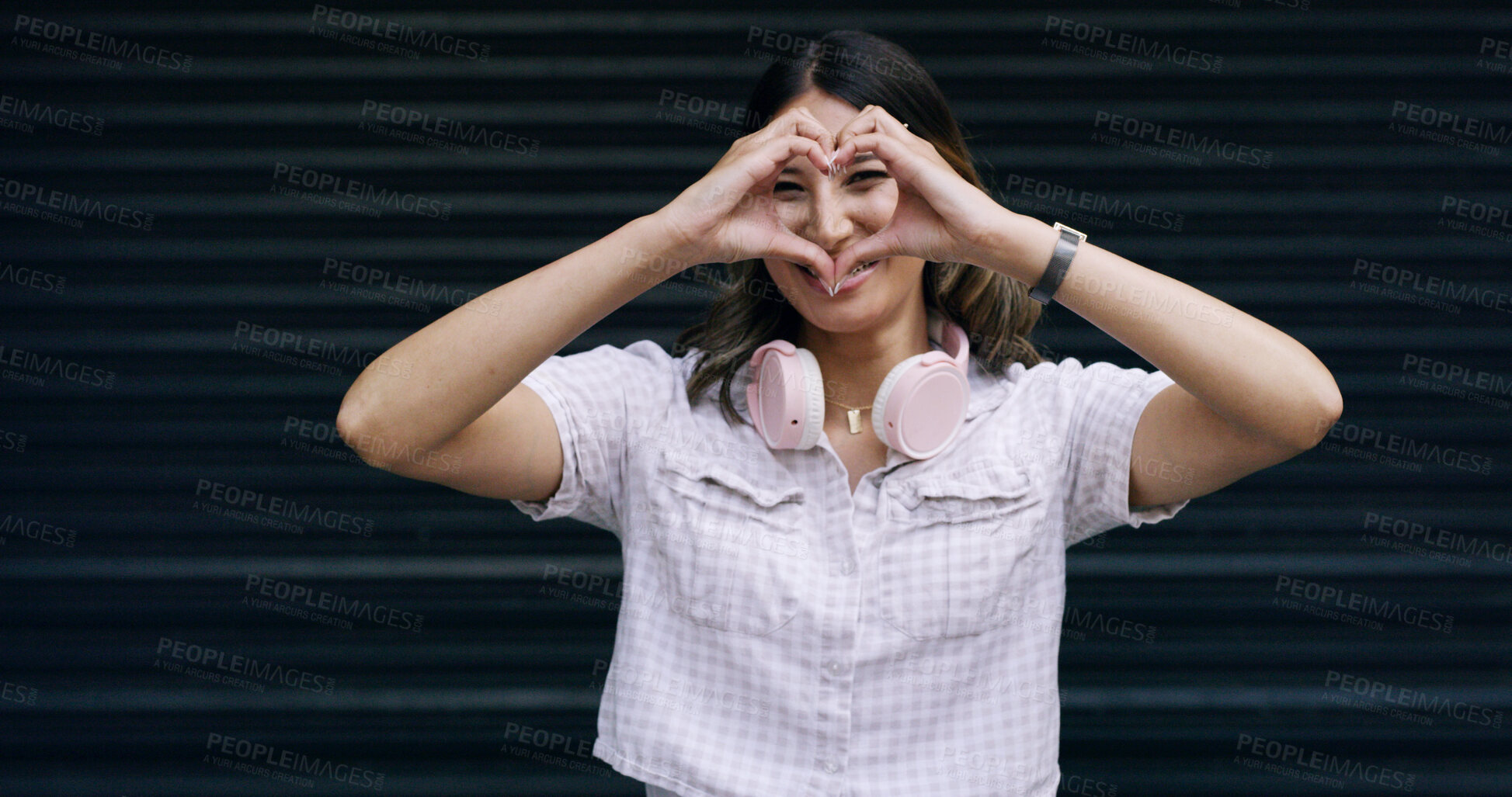 Buy stock photo Happy woman, portrait and sign with heart hands in studio for love on a dark background. Female person, model or gen z with headphones, shape or emoji for romantic gesture, support or care on space