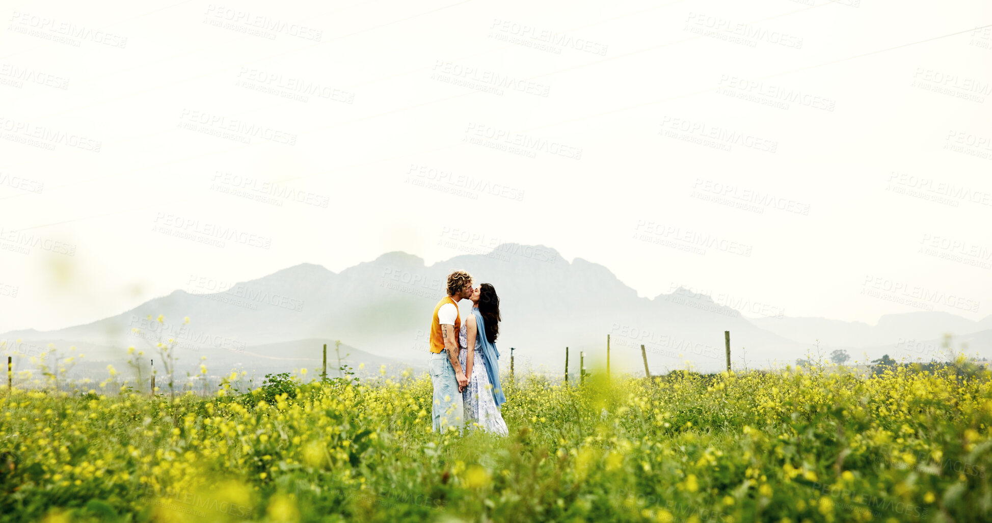 Buy stock photo Love, couple and kiss on field for connection, care and holding hands with space on holiday. Romance, man and woman in countryside with flowers on vacation, commitment and bonding together outdoor