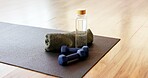 Mat, dumbbells and bottle with towel in yoga studio for fitness challenge, hydration or workout. Kneeling pad, weights or water drink in gym for exercise, physical activity or liquid electrolytes
