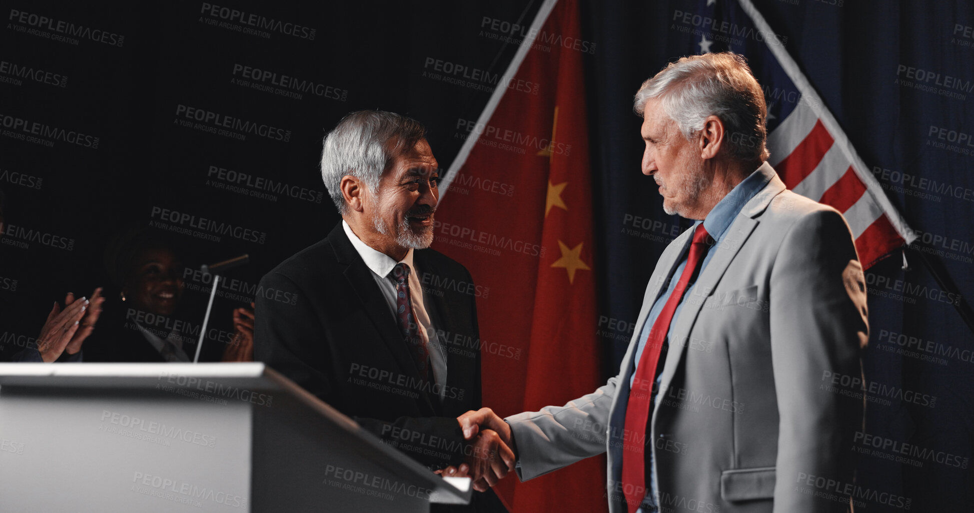 Buy stock photo Men, handshake and flags with agreement, stage or happy for trade partnership, success or tariff deal. People, USA and China with global leader, shaking hands and smile with crowd applause at seminar