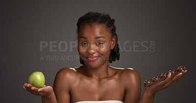 Buy stock photo Apple, chocolate and face of black woman in studio for options or selection of food snack. Choice, fruit and slab with African model on gray background or mockup space for decision, diet and wellness