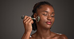 Black woman, skincare and facial treatment with jade roller for massage on a gray studio background. Female person, model or relaxation with spa tool for collagen, circulation or dermatology on space