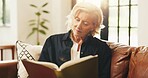 Senior woman, reading book and happy on couch, relax and literature in living room at apartment. Person, smile and novel on sofa in lounge for learning, poetry or fiction story with flare at house