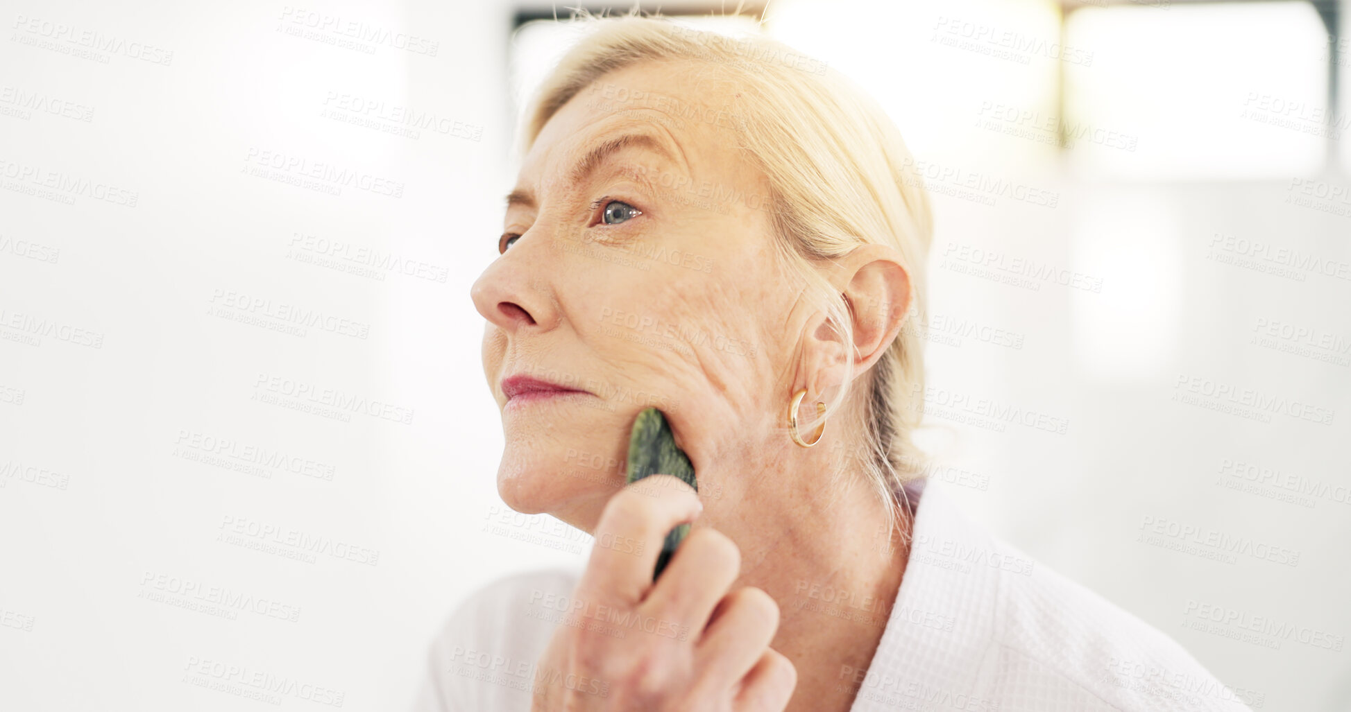Buy stock photo Woman, gua sha and skincare routine in bathroom with tools, circulation or benefits in house. Mature person, anti aging and stone for wrinkles with blood flow, massage and dermatology at apartment