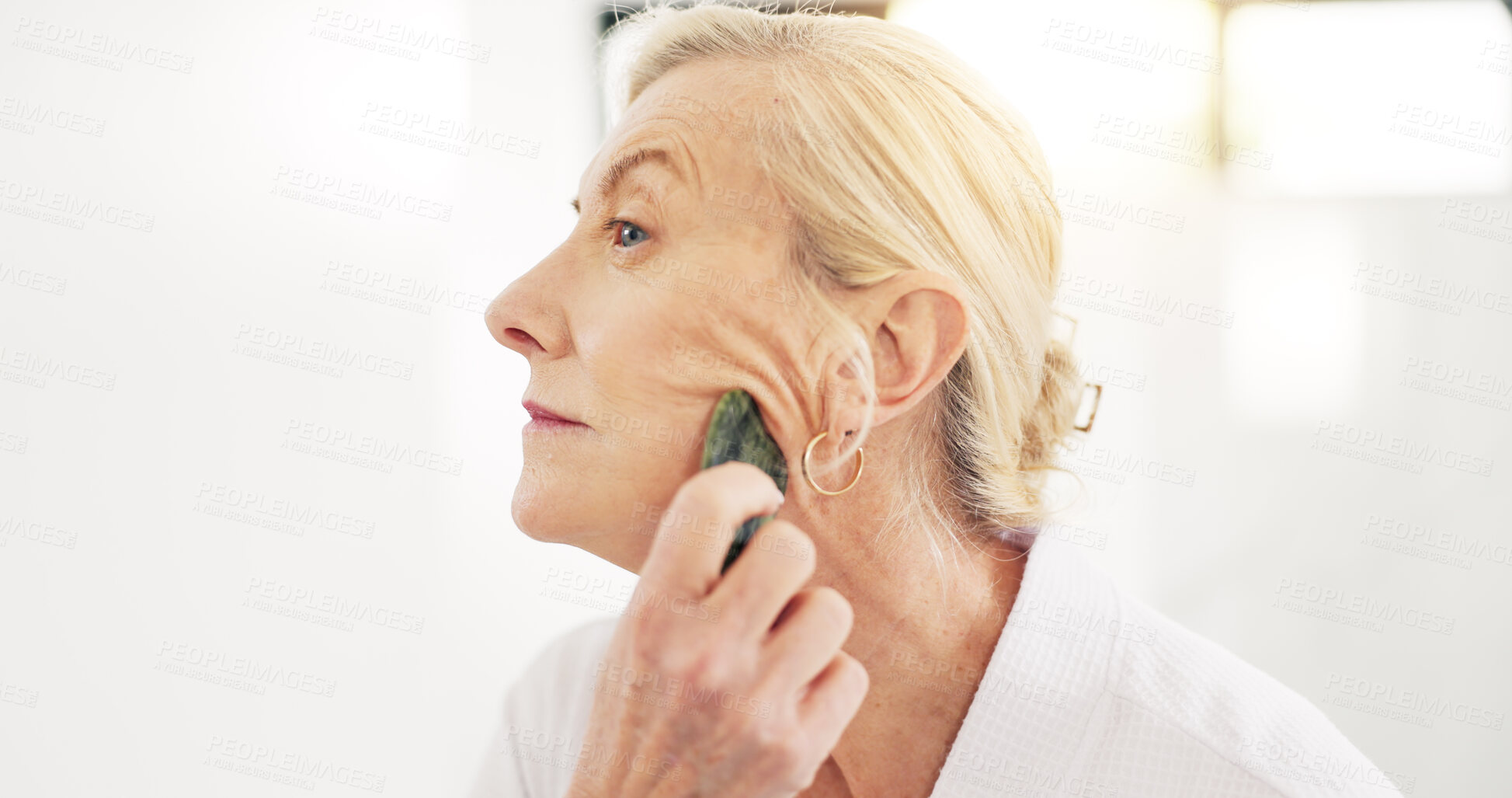 Buy stock photo Woman, gua sha and skincare treatment in bathroom with tools, circulation or benefits in house. Mature person, anti aging and stone for wrinkles with blood flow, massage and dermatology at apartment