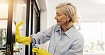 Mature woman, cloth and cleaning window in home for hygiene, bacteria or dirt in morning. Person, chores and chemical with gloves, sanitation or bottle for germs, virus or dust on front door in house