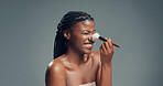 Makeup, beauty and black woman with brush in studio for shine, foundation or glow. Smile, apply cosmetics and model with product for makeover, aesthetic or change with powder on gray background space