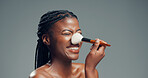 Makeup, beauty and happy black woman with brush in studio for shine, foundation or glow. Smile, apply cosmetics and model with product for facial makeover, change and powder on gray background space