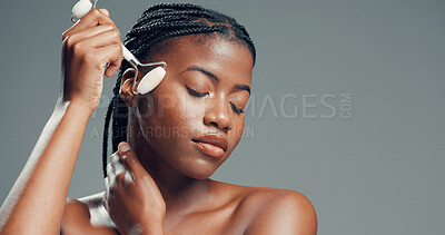 Buy stock photo Face roller, black woman or relax in studio with massage for skincare, dermatology or facial tension. Calm, person or cosmetic tool for lymphatic drainage, wellness or mockup space on gray background