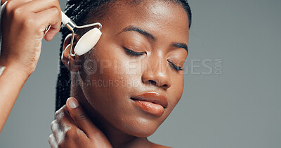 Buy stock photo Face roller, black woman or massage in studio with skincare for beauty, dermatology or facial tension. Person, cosmetic and rose quartz tool for grooming, wellness or mockup space on gray background.