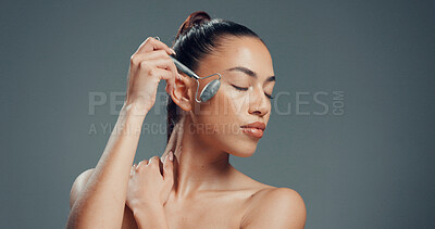 Buy stock photo Beauty, woman and jade roller in studio with massage for skincare, dermatology and facial tension. Relax, person and cosmetic tool for lymphatic drainage, wellness or mockup space on gray background.