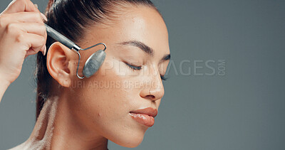 Buy stock photo Woman, jade roller and massage in studio with skincare for beauty, dermatology and facial tension. Relax, person and cosmetic tool for lymphatic drainage, wellness or space on gray background.