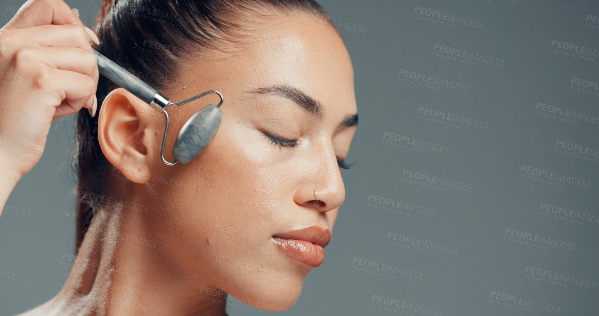 Buy stock photo Woman, jade roller and massage in studio with skincare for beauty, dermatology and facial tension. Relax, person and cosmetic tool for lymphatic drainage, wellness or space on gray background.