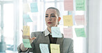 Business, woman or brainstorming at glass wall with sticky note, planning and project management. Thinking, person and employee in office with moodboard for strategy, problem solving and development.