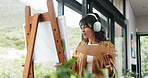 Painting, artist or headphone by window for creativity project, self expression or concentration for craft. Tech, streaming music or mature woman with artistic activity, creation or low angle in home