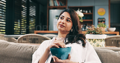 Buy stock photo Eating, relax and thinking with woman on sofa in living room of home for hunger or nutrition. Bowl, snack and vision with happy Indian person chilling in apartment for break, diet or weekend me time