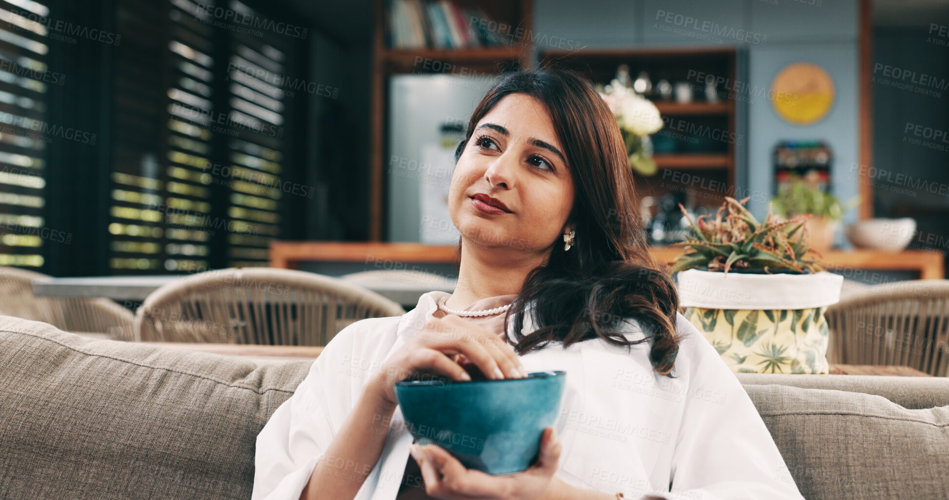 Buy stock photo Eating, relax and thinking with woman on sofa in living room of home for hunger or nutrition. Bowl, snack and vision with happy Indian person chilling in apartment for break, diet or weekend me time