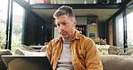 Laptop, remote work and research with man on sofa in living room of home for online planning. Computer, email and typing with mature freelance employee in apartment for small business startup