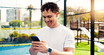 Happy, man and reading with phone on tennis court with fitness app, training tips and track progress. Person, mobile and reservation for padel, technique and video demonstration of tournament results