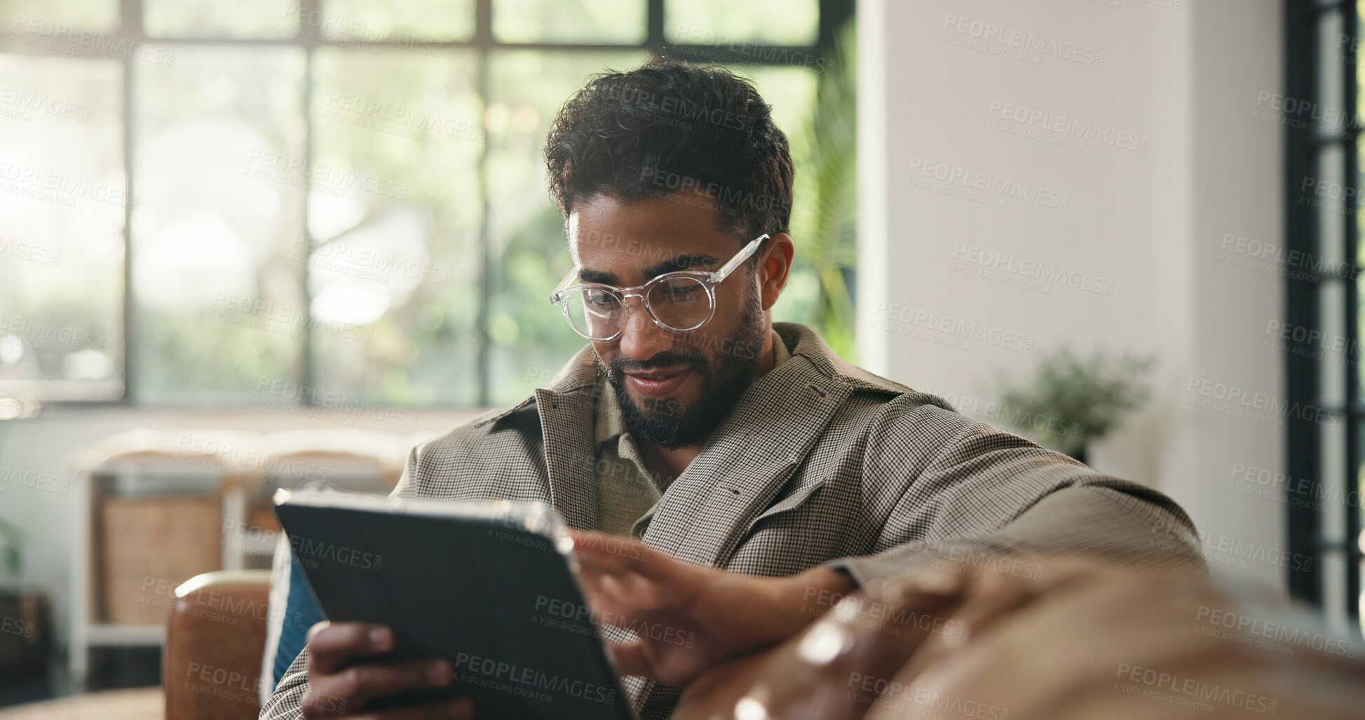 Buy stock photo Creative, online and man with tablet, home or reading draft on web, scroll and remote work in lounge. Review, story and person with glasses for editing, happy and self publisher with tech for ebook