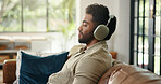 Headphones, relax and man on sofa in home listening to music, playlist or radio in living room. Happy, audio tech and male person streaming song, album or podcast for chilling on weekend in house.
