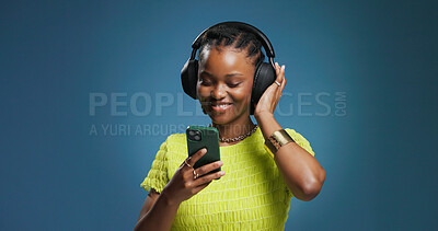 Buy stock photo Headphones, phone and black woman in studio with music, radio or song for rhythm and energy. Happy, audio tech and African person listening to album on cellphone with mobile app by blue background.