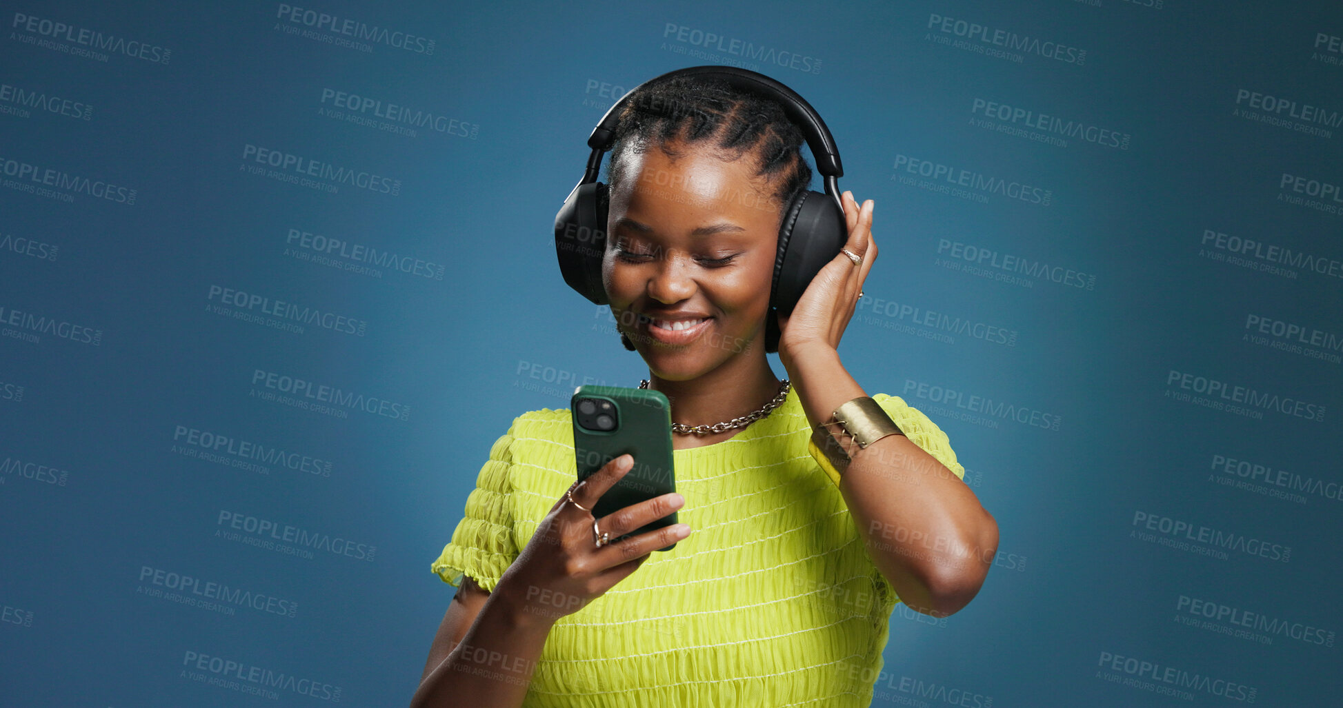 Buy stock photo Headphones, phone and black woman in studio with music, radio or song for rhythm and energy. Happy, audio tech and African person listening to album on cellphone with mobile app by blue background.