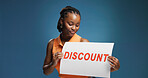 Happy, black woman or discount with sign for marketing or advertising on a blue studio background. Female person, promoter or model with poster or billboard for offer, shopping deal or price decrease