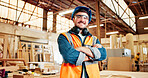 Carpentry, crossed arms and portrait of man in factory for furniture repair, restoration and woodworking. Carpenter, safety gear and happy person in workshop for wood, lumber and timber production