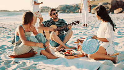 Buy stock photo Happy people, friends or playing with guitar on beach for picnic, music or social gathering. Group, community or gen z with playful musician or acoustic instrument on ocean coast for fun outdoor meal