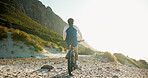 Man, bicycle and cycling with mountain for fitness, journey or outdoor adventure in nature. Back view, male person or cyclist with bike on rocky shore for exercise or ride on space in wilderness