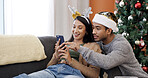 Christmas, phone and couple relax in home for gift shopping, pointing and decision online. Xmas, man and woman with mobile in living room for holiday sale, e commerce and smile for festive discount
