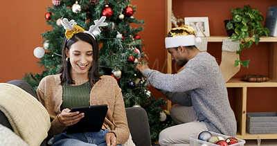 Buy stock photo Christmas, smile and tablet with woman on sofa in living room of home for decoration ideas. App, festive and person in lounge with man decorating tree for celebration, season or tradition as couple
