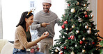 Christmas, tree and happy couple with ornament in home, holiday tradition or decoration for bonding. Festive activity, string lights or people with bauble in lounge, celebration preparation and smile