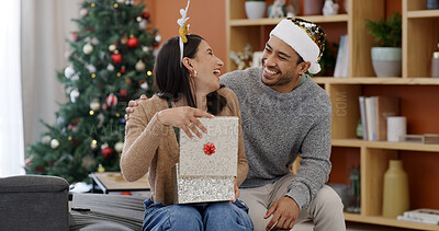 Buy stock photo Christmas, couple and laugh in living room with gift for holiday tradition, connection and gratitude. Happy, married people and present in house for festive season, appreciation and bonding together.