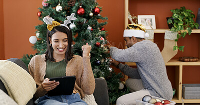 Buy stock photo Christmas, fist pump and tablet with woman on sofa in living room of home for decoration success. App, celebration and person in lounge with man decorating tree for season or tradition as couple