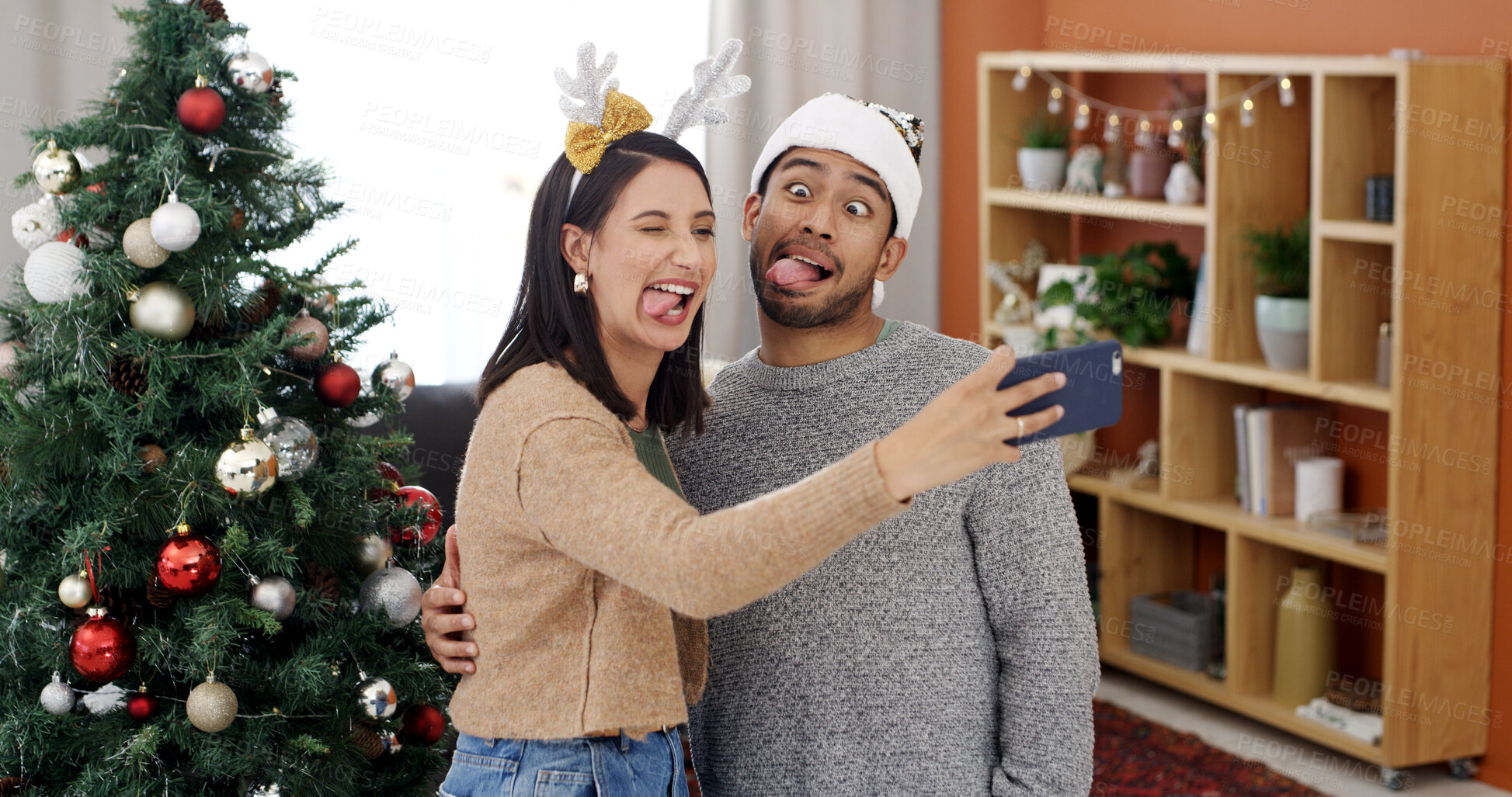 Buy stock photo Christmas, funny face and selfie of couple in home for holiday memory, social media post or comic. Man, woman and photo on xmas in living room together for festive celebration, goofy and tongue out