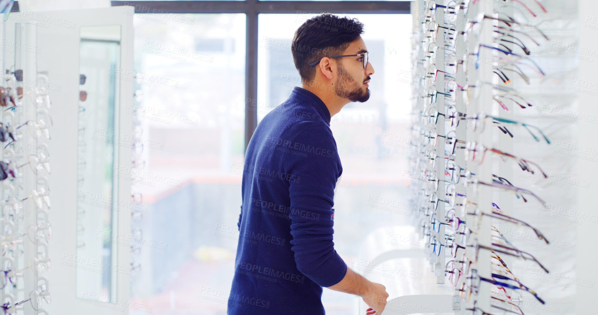 Buy stock photo Eye care, man and customer shopping for glasses, vision and eyesight improvement with choice. Store, eyewear and person with frame for optometry, check spectacles and lens for health at shelf