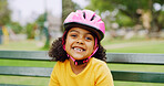 Helmet, portrait and smile of girl child on park bench for activity, hobby or responsibility. Protection, safety and youth with excited kid outdoor in nature for development, learning or motor skills