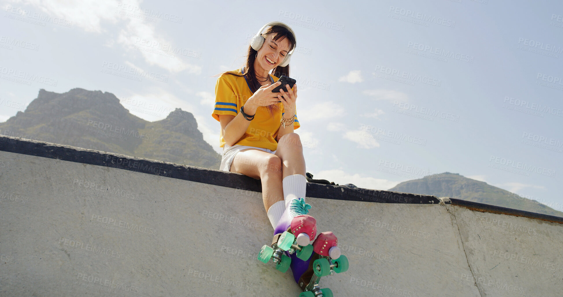 Buy stock photo Woman, roller skates and phone at park with smile, headphones or listen to music with space in city. Person, skater and smartphone for streaming subscription, low angle or relax on ramp in urban town