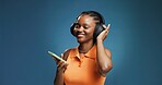 Headphones, smile and black woman in studio with phone, listening and music playlist. Happy, audio tech and African female person with groove for album, radio or song for rhythm on blue background