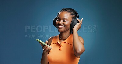 Buy stock photo Headphones, smile and black woman in studio with phone, listening and music playlist. Happy, audio tech and African female person with groove for album, radio or song for rhythm on blue background