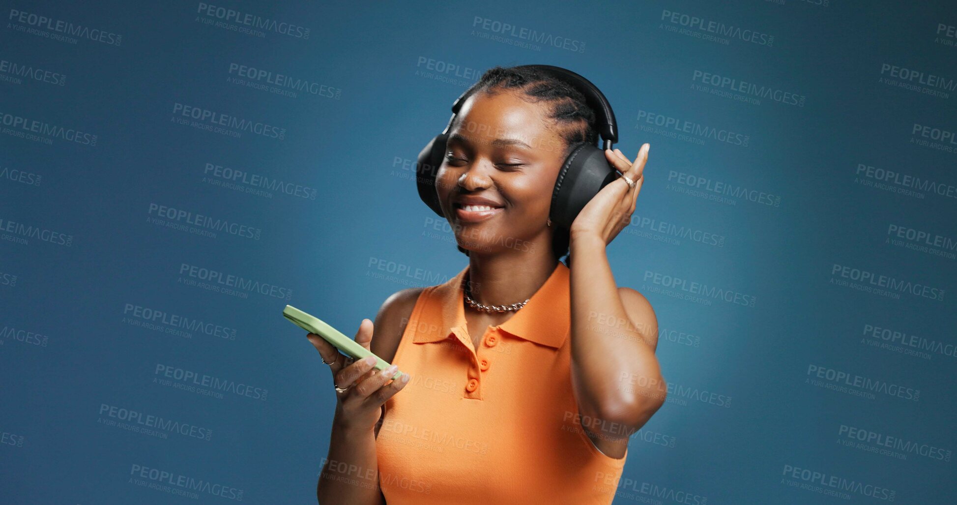 Buy stock photo Headphones, smile and black woman in studio with phone, listening and music playlist. Happy, audio tech and African female person with groove for album, radio or song for rhythm on blue background