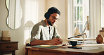 Headphones, remote work and writing with man in home office for journalism or publication. Music, notebook and pen with freelance journalist at desk in study of apartment for article research