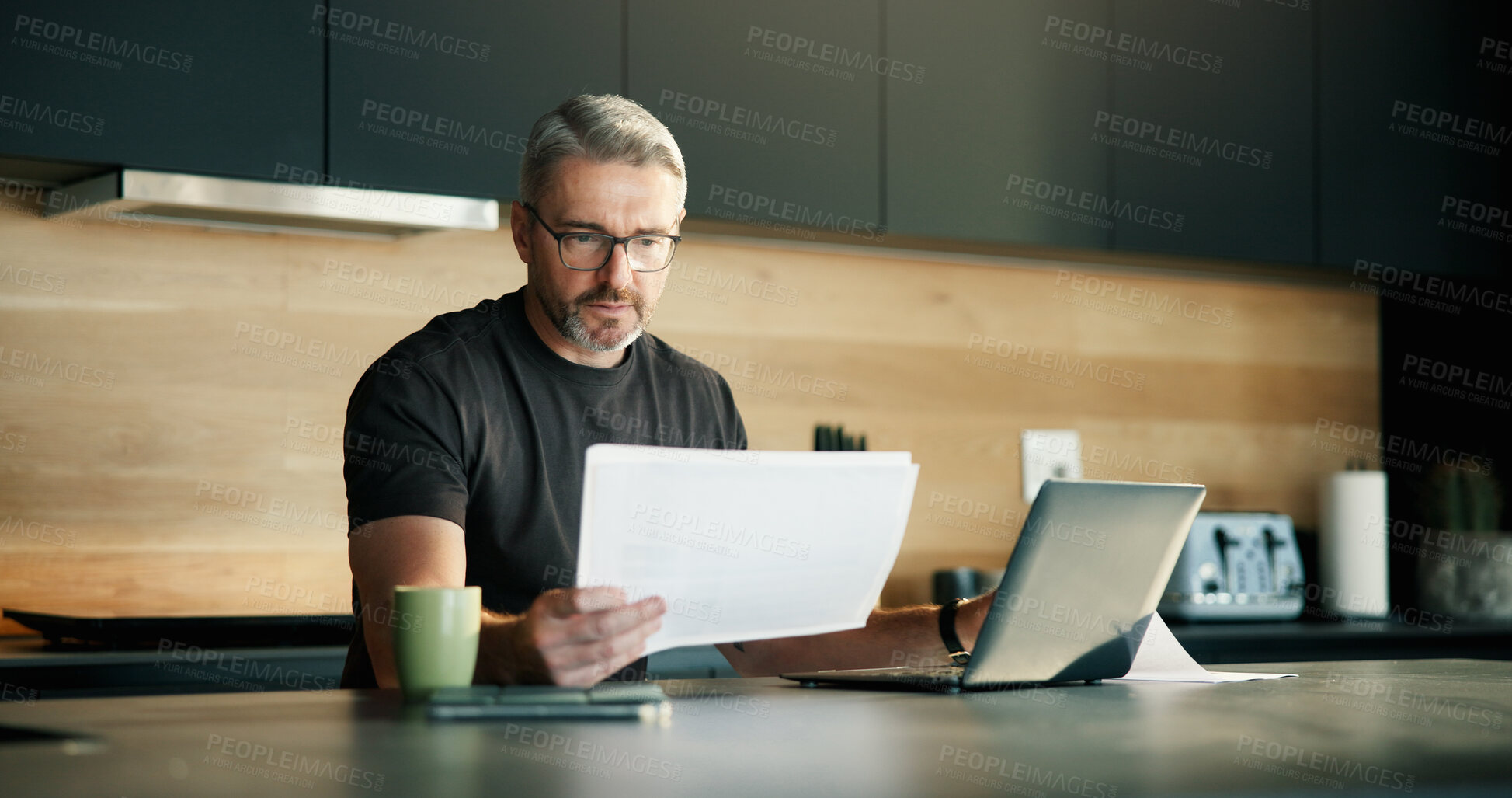 Buy stock photo Documents, laptop and remote work with man in kitchen of home for planning, report or research. Computer, paperwork and reading with mature freelancer in apartment for schedule or startup review