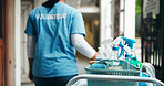 Back. person and volunteer with supplies for cleaning, corridor maintenance and facility hygiene. Woman, trolley and hallway cleanliness with equipment, chemical detergent and sanitation for outreach